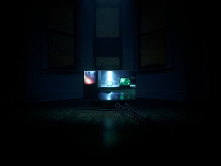 Dark room with a large screen displaying multiple smaller screens, evoking Memento Mori