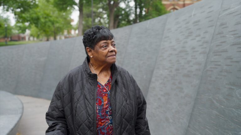 Sarah Ann Kelley stands beside a curved memorial wall, looking thoughtfully to the side.