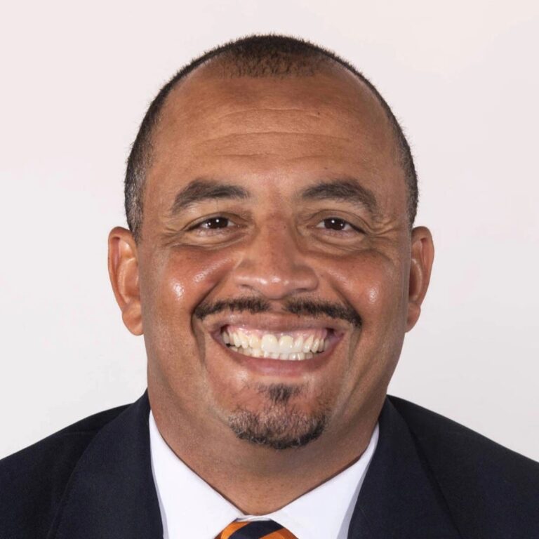 Headshot of Tony Elliott, smiling broadly, wearing a dark suit and tie.
