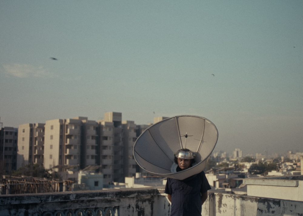 Man wearing satellite dish on head on rooftop, WE WERE HERE