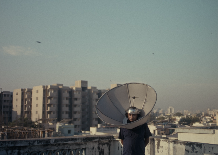 Man wearing satellite dish on head on rooftop, WE WERE HERE