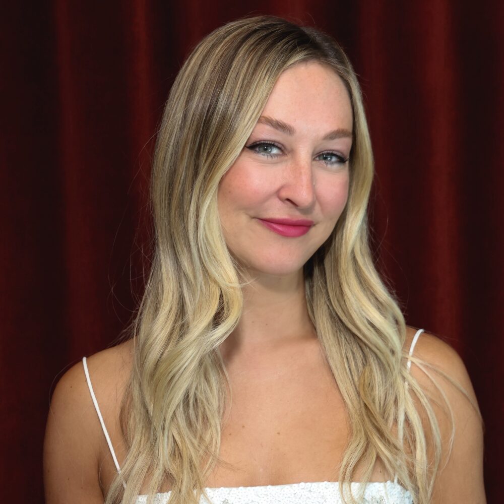 Whitney Fern smiles in a white dress against a red backdrop.