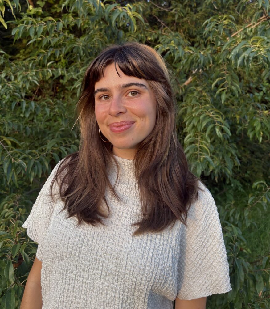 Laura May Brunk smiles outdoors in front of lush green foliage
