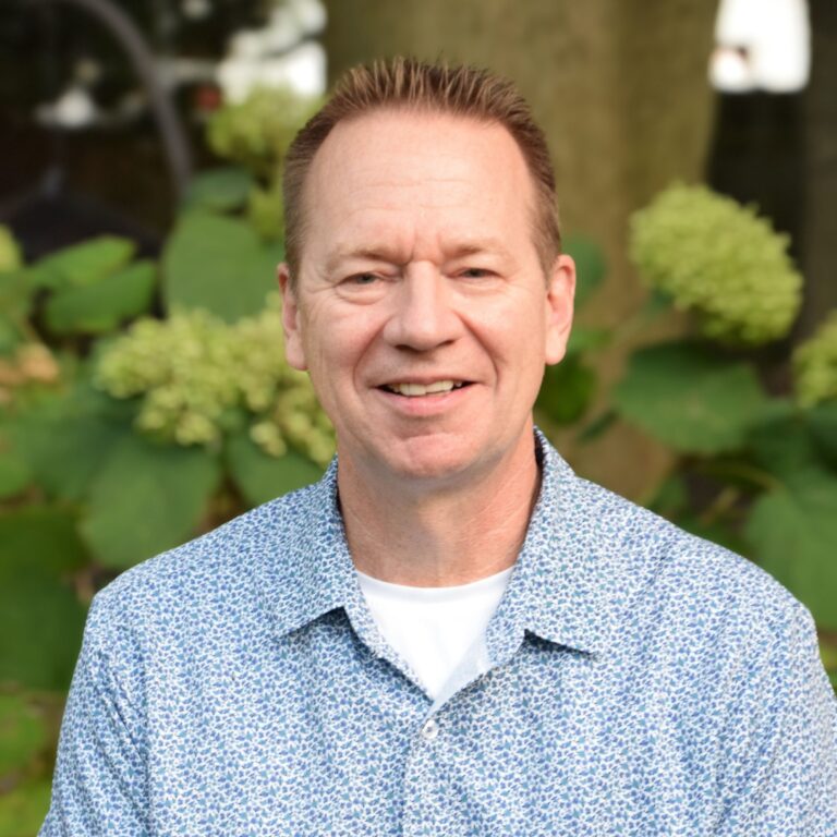 Greg Frith smiling in front of green foliage