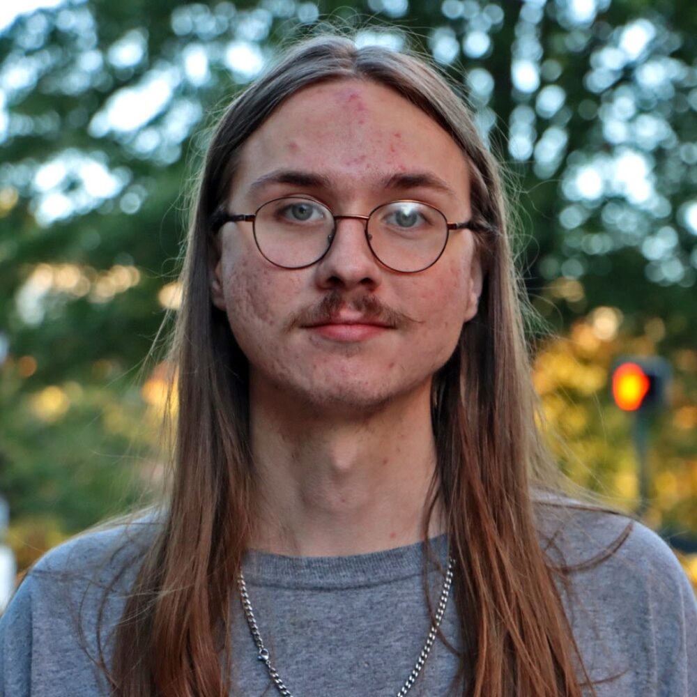 Luke Headley portrait with glasses and long hair outdoors